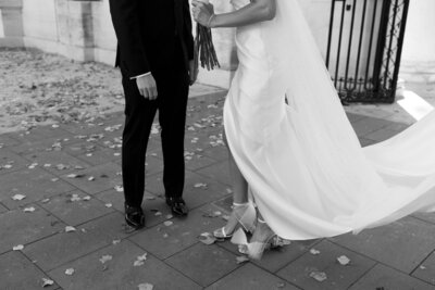Close up of a couple's wedding attire from shoulders down. Person in a black suit and in a white wedding dress and heels