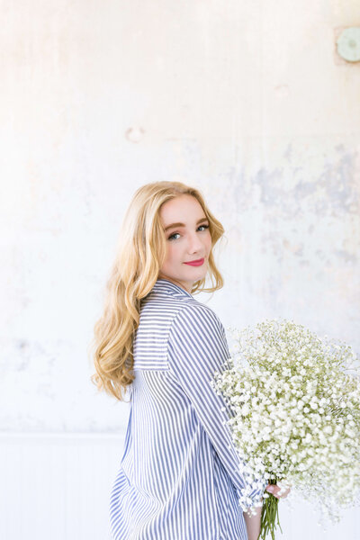 blonde girl with red lip stick and a blue striped button up hold a baby's breath bouquet in a photography studio