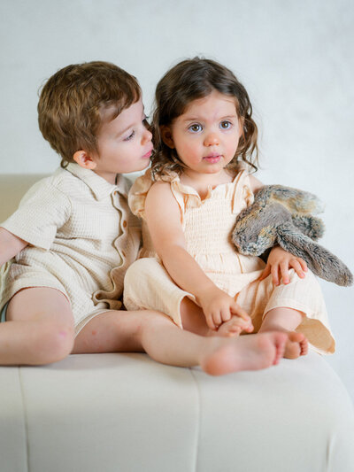 sibling brother kissing little sibling sister on the cheek while see looks at her parents