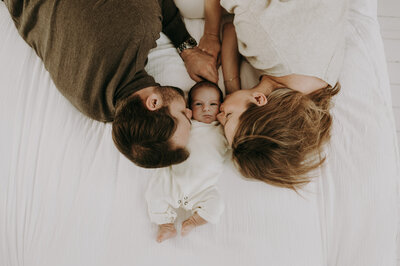 Koppel ligt met baby op het bed en geven de baby een kus.