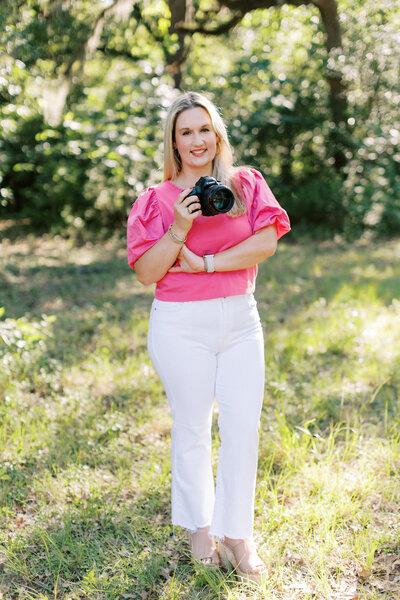 woman in white pants and a hot pink top holding a camera