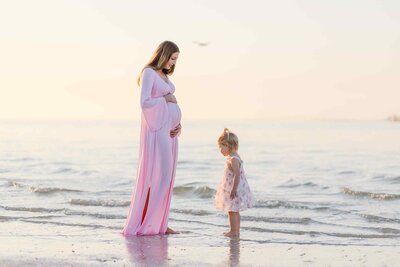Pregnant mom looks down at young daughter on the beach