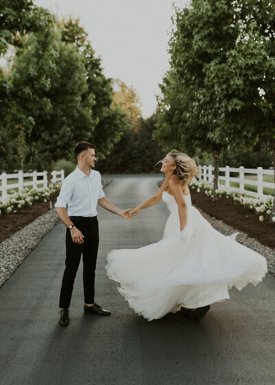 Groom spinning bride in wedding dress in the middle of a tree lined road
