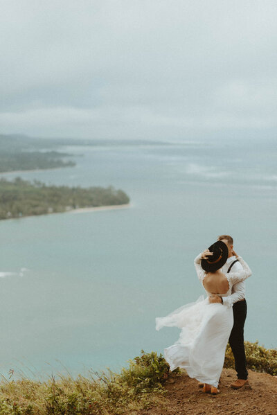bride and groom standing on windy cliff