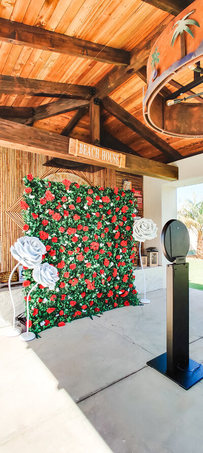 Red and green flower wall backdrop with oversized white roses and photo booth setup at an outdoor Arizona venue by Stars and Stripes Events LLC.