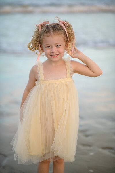 little girl in pig tails and yellow dress, playing in ocean during a family photo shoot on the beach near Orlando taken by Melissa Vinsik Photographer