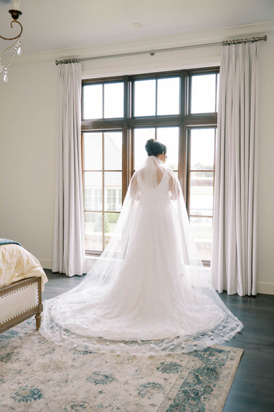 Bride in lace gown standing by tall estate windows during a refined Southern garden wedding in Oklahoma