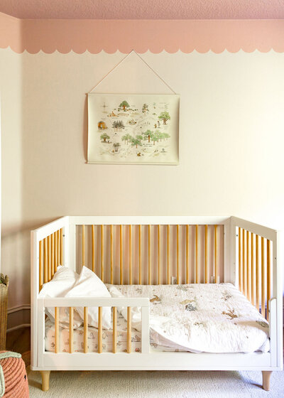 A child's room with painted scallops on the wall above a kid's bed.