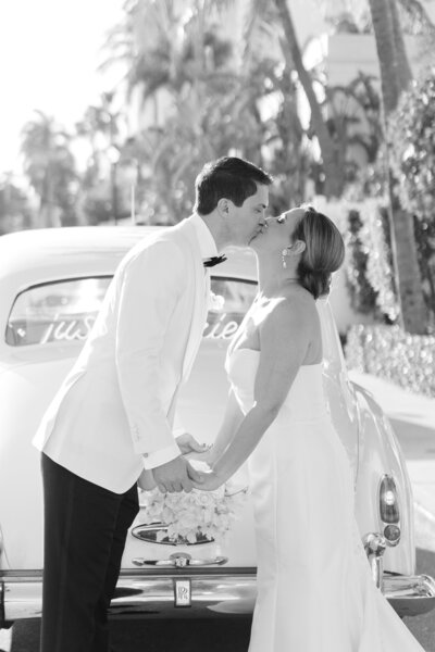Bride and groom kiss in front of classic getaway car