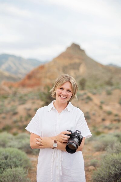St. George  family photographer girl standing in the sand at sand hollow state park holding the camera and smiling