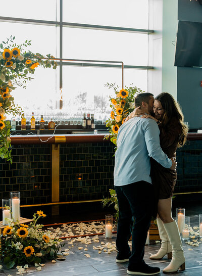 Couple embracing in front of a romantic sunflower arch with candles and rose petals, styled proposal setup by Yours Truly, a wedding planner and designer in New Jersey.
