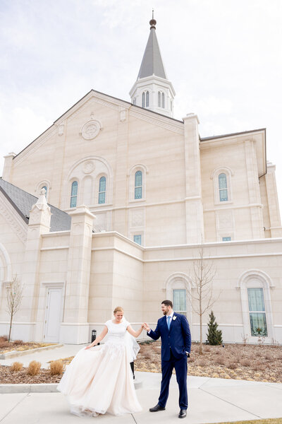  Groom twirls his bride playfully outside the Taylorsville Utah Temple during their wedding photoshoot.