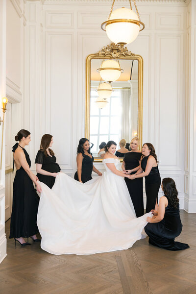 Portrait of the bride in timless wedding dress with her bridesmaids around in black dresses at The Adolphus in Dallas