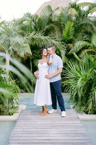Couple embracing in a lush tropical garden, framed by palm trees and greenery.