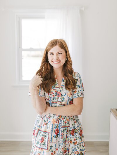 Women wearing a floral dress smiling and standing in her studio.