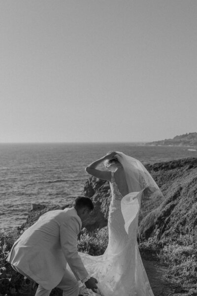 Groom fixes brides dress while standing on Big Sur Cliffside
