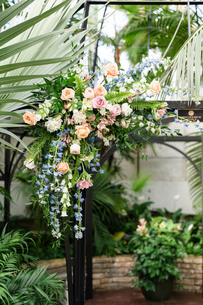 An elegant pastel floral arrangement hangs on the altar for a wedding at the Franklin Park Conservatory Palm House