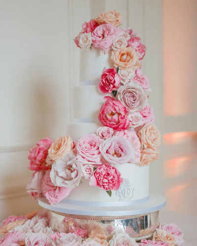 A wedding cake full of pale flowers running down the length of the cake