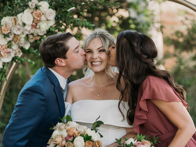 bride smiling being kissed on either cheek by her brother and sister-in-law  at blomgren ranch captured by los angeles wedding photographer magnolia west photography