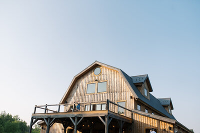 Rustic wooden barn-style event venue with upper-level deck and large windows, captured at golden hour at Bear Ridge Destination.