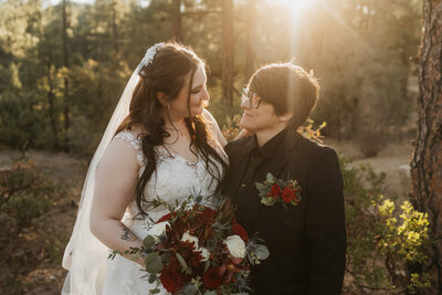 A newlywed couple standing close and looking at each other in a forest 