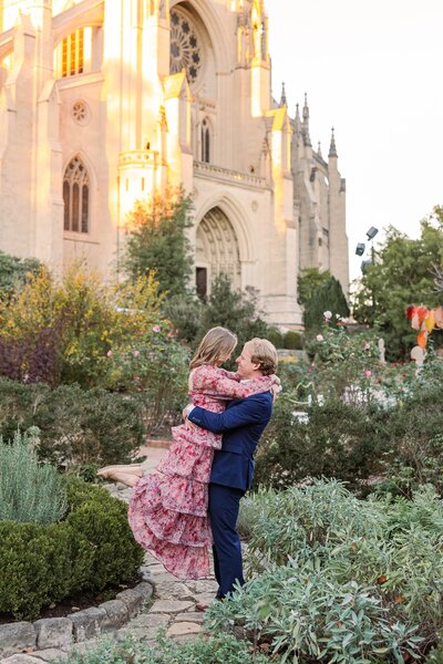 Romantic engagement session at Bishop’s Garden, Washington National Cathedral in DC, with couple embracing amidst blooming gardens and iconic gothic architecture