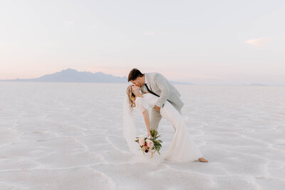 Bride and groom kiss while groom dips back bride on the Bonneville salt flats of Utah
