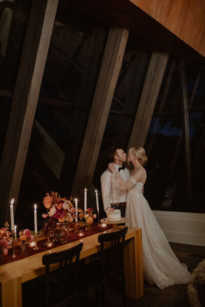 Bride and groom kiss in front of their candlelit dinner table