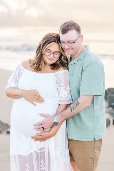 expecting parents snuggling looking at the belly at the beach