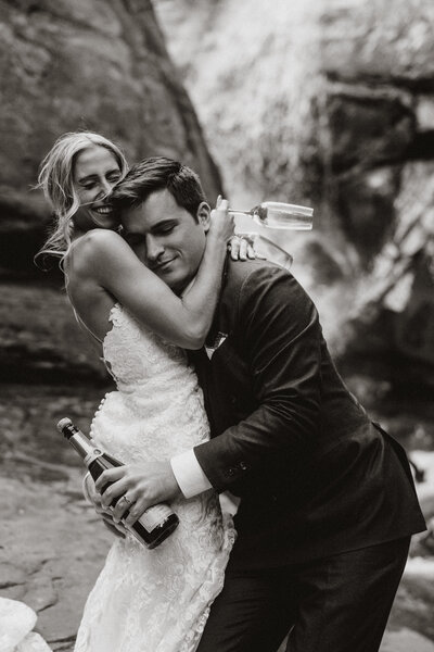 Bride and groom pop champagne and embrace near a waterfall at their Breckenridge elopement.