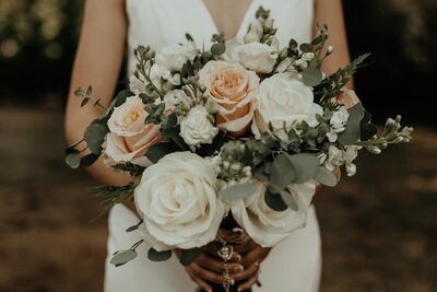 A bridal bouquet of white and peach roses held by a bride in her wedding dress