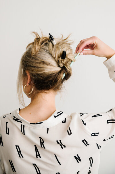 The back of Sarah Klongerbo pulling her hair up with pens