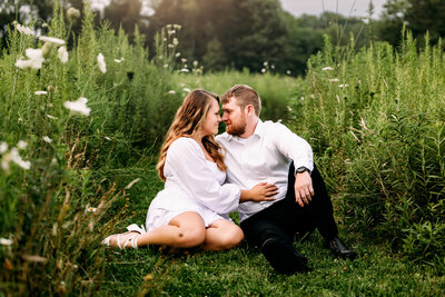 Couple snuggles affectionately while sitting in a picturesque field surrounded by tall grass