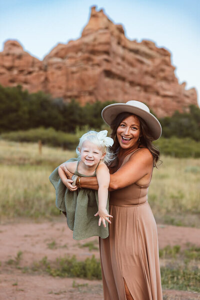 Mom in hat airplanes her young daughter toward camera out at South Valley Park.