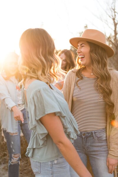 a group of women are laughing while one looks over her shoulder during golden hour in  surf city, north carolina