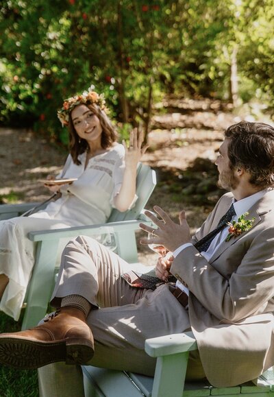Grinning bride holding up her hand to display her new wedding band to her husband as they sip wine in the sun at The Madrones in Anderson Valley