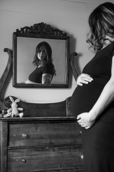 Black & White Photo of Expecting Mom holding belly looking in mirror
