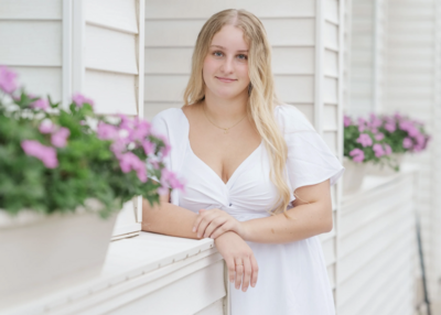 a girl in a white dress smiling while standing next to flowers in a window box