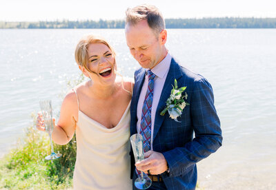 Bride and groom laughing together in front of a lake in Calgary, Ab.