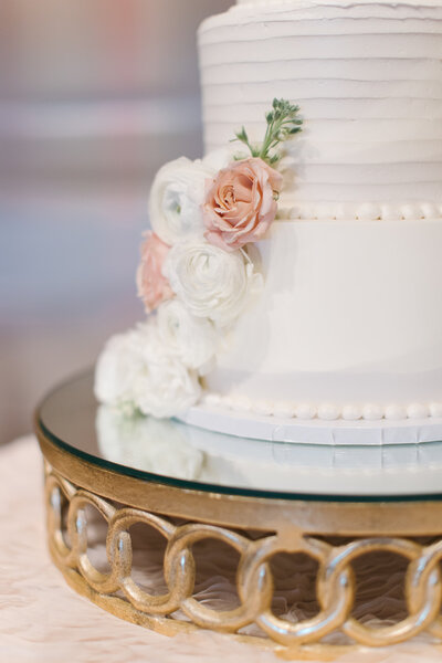 Detail shot of white wedding cake with blush florals and gold mirrored base, part of a refined dessert display by The Eventful Gals.