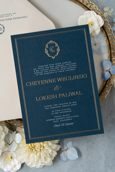 White wedding invitations with black serif text tied with string on a table with tan envelopes and rings