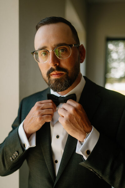 Two partners share an intimate moment in a warmly lit room during their downtown Tucson, Arizona wedding. One partner is seated, while the other stands beside them, resting a hand on their shoulder. The room is adorned with framed artwork and vintage decor.