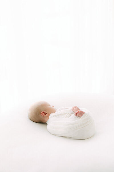 Newborn baby swaddled in white lays with feet out of wrap during portrait session with Indianapolis newborn photographer