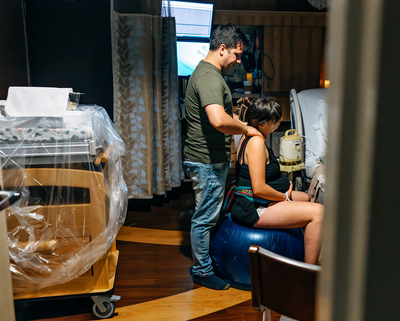 A woman in labor sits on a birth ball while her husband rubs her shoulders