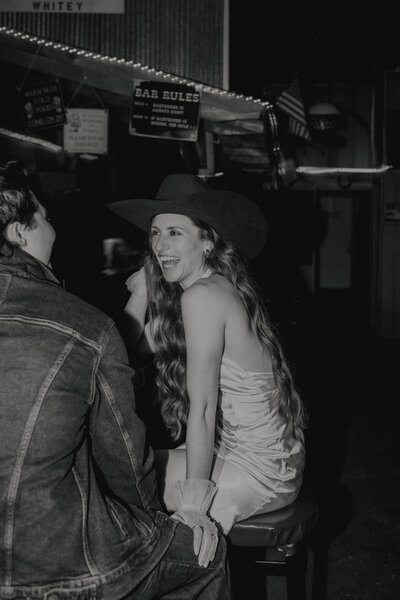 couple laughing to while bride wears grooms cowboy hat