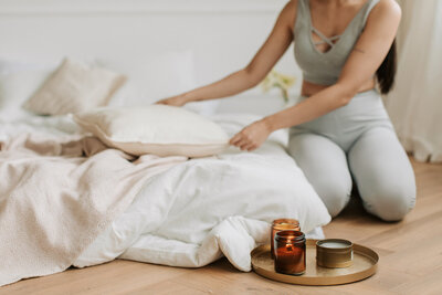 A woman kneeling next to white bedding and candles. Showing a type of stress management that might be suggested by a counselor in New York. Get more support for overwhelm with stress counseling in NYC.