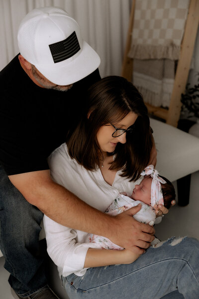mama craddling newborn in her arms dad has his arms wrapped around mama