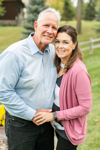 An older white couple is standing close together facing the camera and smiling