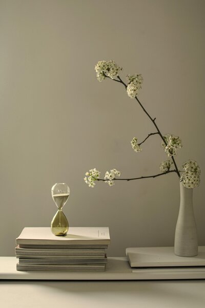 Desk with an hourglass, several books and a modern vase with white flowers