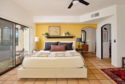 Bright primary bedroom of a home in Cave Creek, Arizona. Yellow wall, southwester decor and a patio through a sliding door.